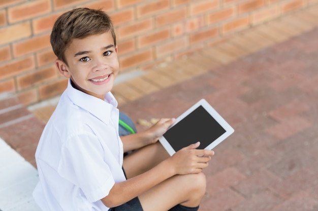 Estudante feliz sentado no corredor e usando tablet digital