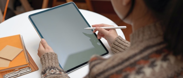 Estudante feminino fazendo tarefa com tablet mock-up vertical e artigos de papelaria na mesa de café