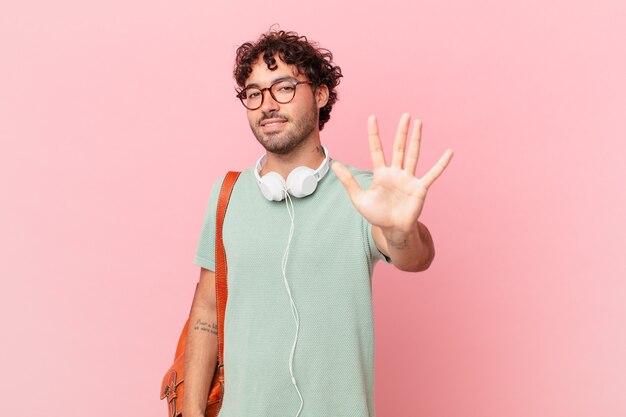 Estudante hispânico sorrindo e parecendo amigável, mostrando o número cinco ou quinto com a mão para a frente, em contagem regressiva