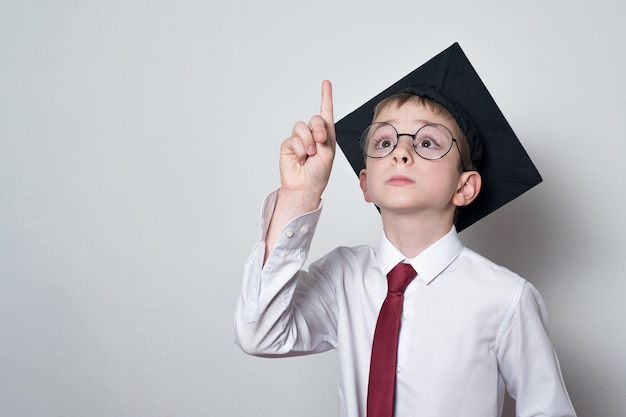 Estudante inteligente com chapéu acadêmico levantou o dedo indicador. Graduando-se criança estudante.