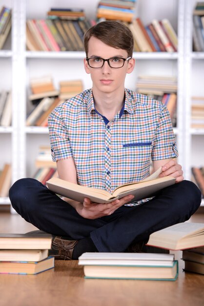 Estudante inteligente com livro aberto, lendo na biblioteca da faculdade