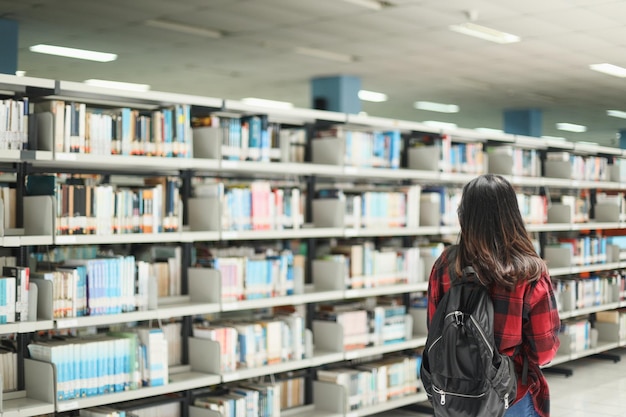 Estudante inteligente em estilo casual usando mochila andando pela biblioteca enquanto procurava um livro