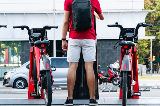 Foto estudante irreconhecível, jovem alugando uma bicicleta em uma cidade grande