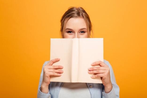 Estudante jovem feliz, cobrindo o rosto com o livro