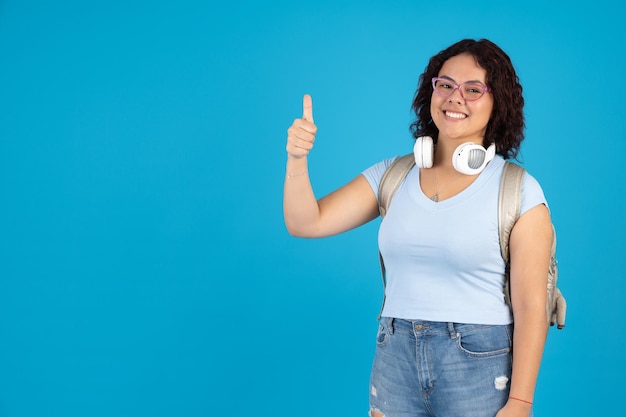 Foto estudante jovem feliz com óculos mostrando um polegar para cima em acordo carregando uma mochila dourada