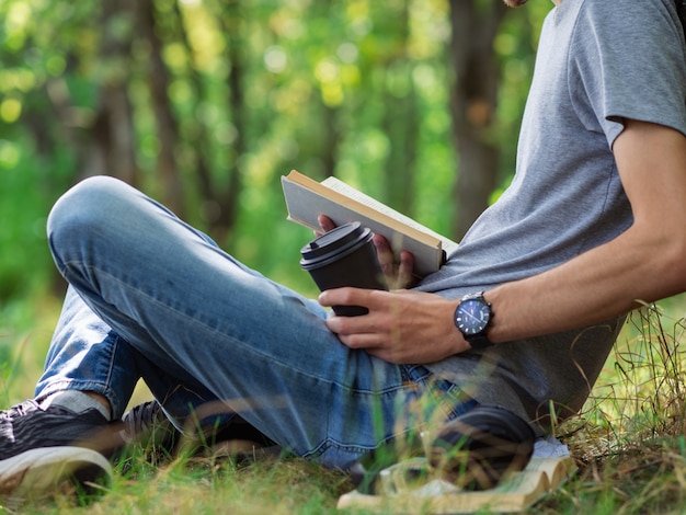 Estudante jovem lendo um livro e se preparando para os exames, sentado na grama do parque.