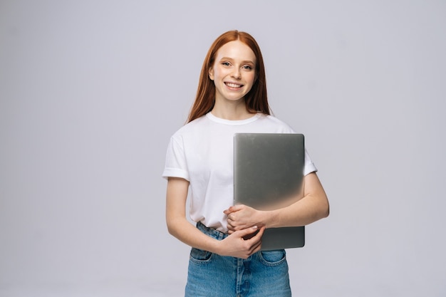 Estudante jovem sorridente segurando um laptop e olhando para a câmera em um fundo isolado