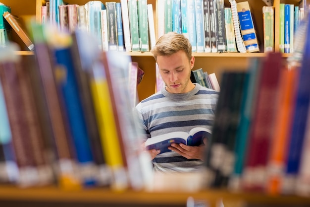 Estudante masculino lendo um livro na biblioteca