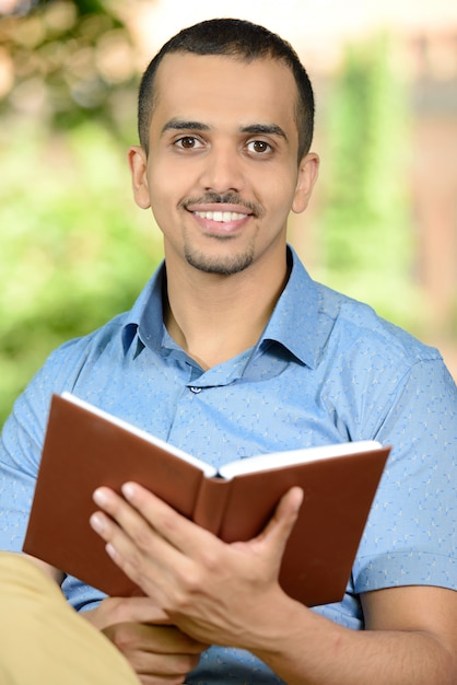 Estudante masculino novo que lê um livro ao ar livre no parque.