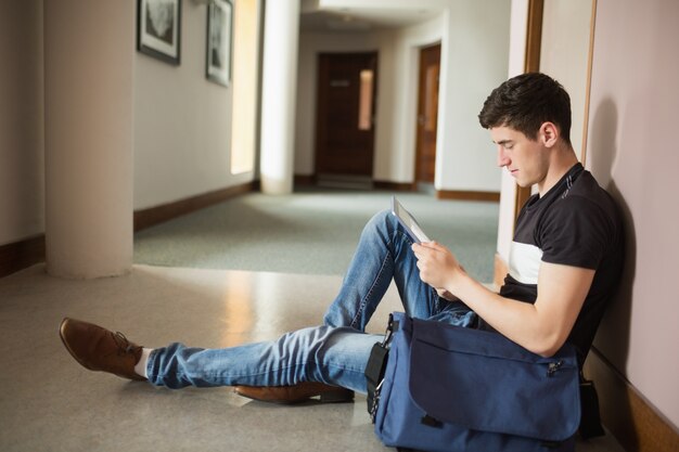 Estudante masculino usando tableta digital sentado por parede