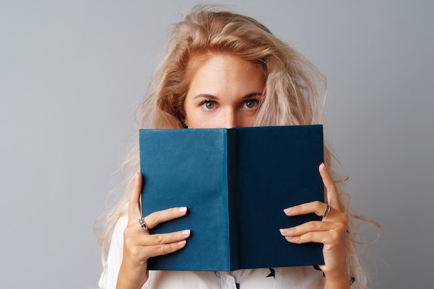 Estudante menina adolescente segurando um livro nas mãos dela sobre um fundo cinza