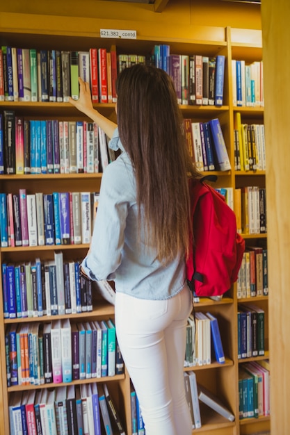 Estudante morena sorridente, escolhendo o livro na biblioteca