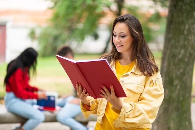 Estudante mulher segurando um livro na frente de um grupo de amigos