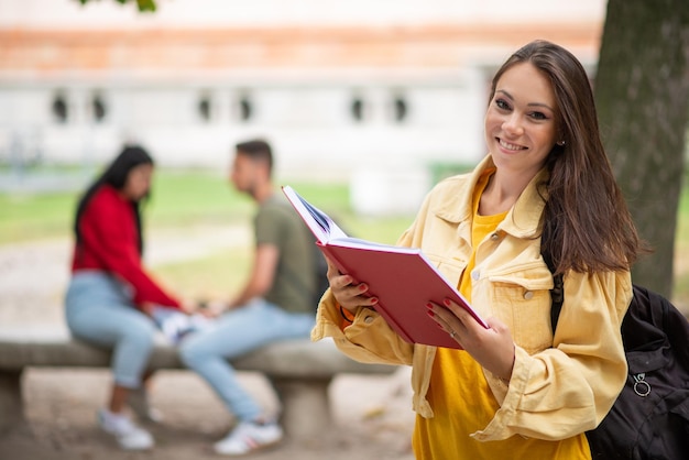 Estudante mulher segurando um livro na frente de um grupo de amigos