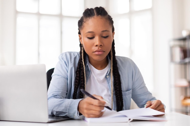 Estudante negra concentrada a estudar com um portátil e um caderno