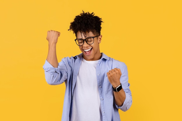 Foto estudante negro exuberante celebra o sucesso em fundo amarelo