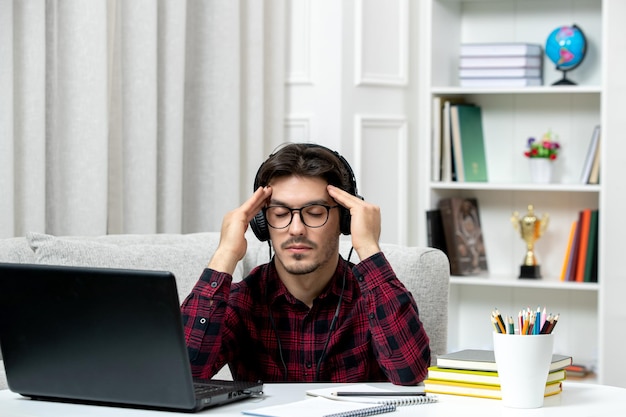 Estudante on-line bonitinho de camisa xadrez com óculos estudando no computador segurando templos