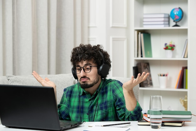 Estudante on-line bonito jovem estudando no computador em óculos de camisa verde acenando com as mãos