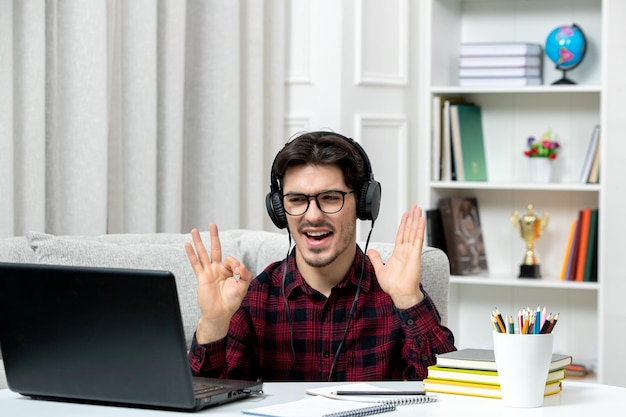 Estudante online jovem de camisa xadrez com óculos estudando no computador acenando com as mãos