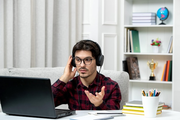 Estudante online jovem de camisa xadrez com óculos estudando no computador confuso acenando as mãos