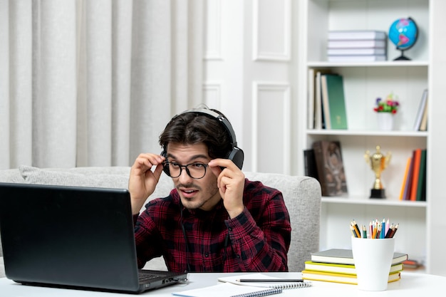 Estudante online jovem de camisa xadrez com óculos estudando no computador olhando focado