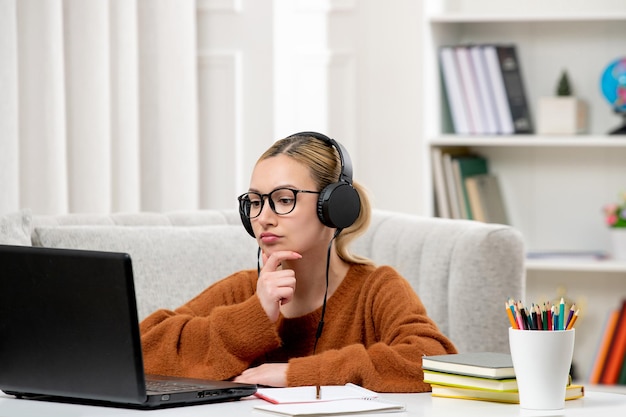 Estudante online jovem linda de óculos e suéter laranja estudando no pensamento do computador
