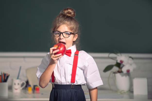 Estudante pequena colegial na classe comendo maçã na educação escolar aprendendo e crianças conc