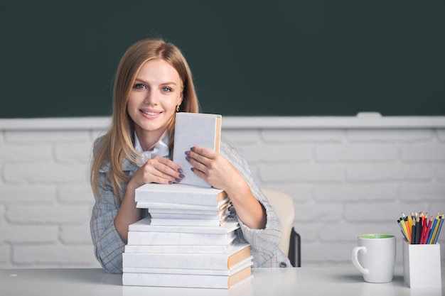 Estudante preparando o exame e aprendendo lições na sala de aula da escola Linda estudante com livros no fundo do quadro-negro com espaço de cópia