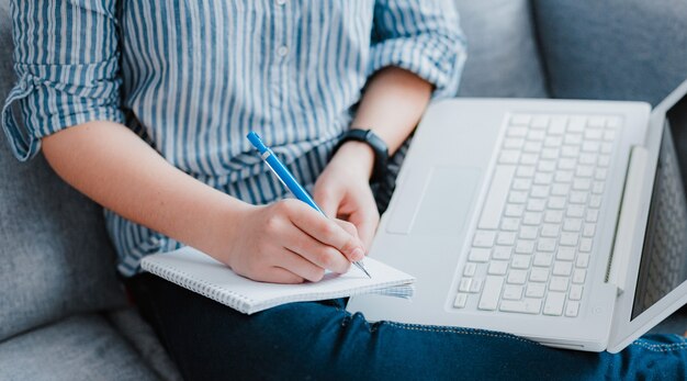 Estudante que estuda em casa trabalhando com seu laptop fazendo trabalhos de casa close-up. Educação a distância de conceito durante a quarentena