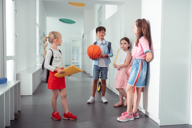 Estudante segurando bola de basquete falando com meninas na escola