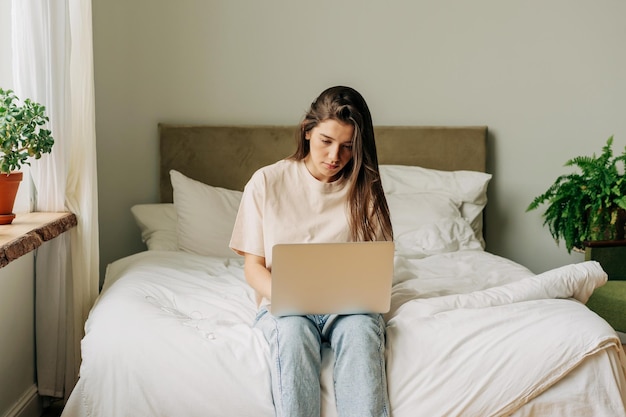 Estudante sentado na cama digitando projeto em laptop aprendendo on-line trabalho remoto de casa