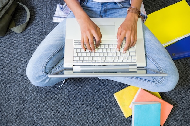 Estudante sentado no chão em biblioteca usando laptop