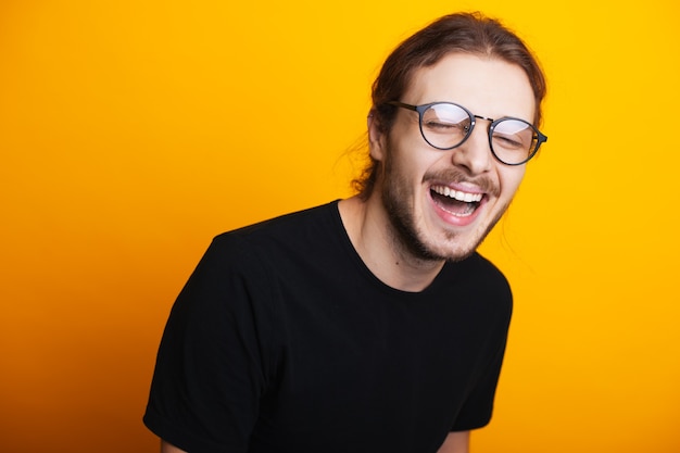 Estudante sorridente, caucasiana, com a barba por fazer, óculos e cabelo comprido posando