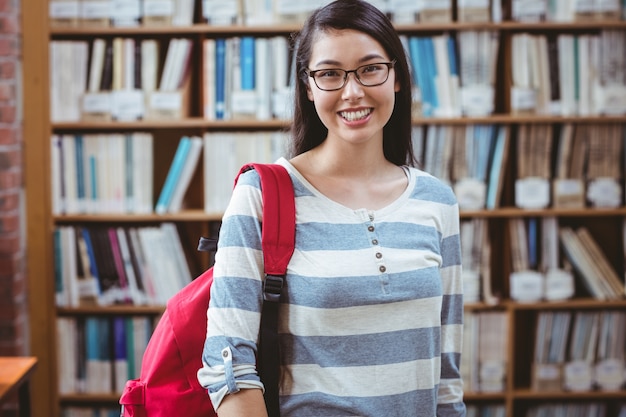 Estudante sorridente com mochila em pé na biblioteca