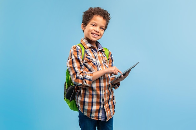 Foto estudante sorridente com tablet e mochila de fundo azul