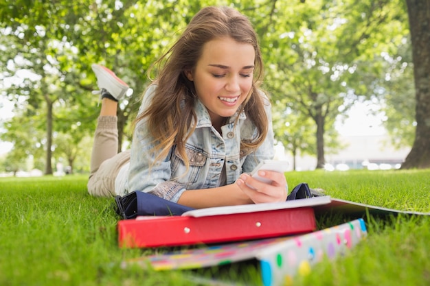 Estudante sorridente que está deitado na grama enviando um texto