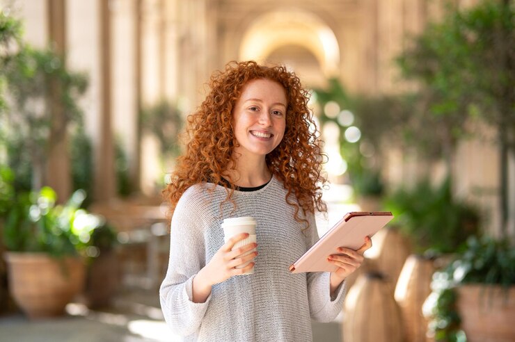 Estudante sorridente segurando café e tablet no claustro da universidade