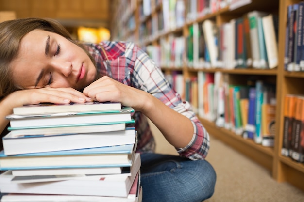 Estudante sorridente sentado no chão da biblioteca apoiado na pilha de livros