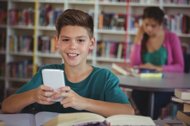 Foto estudante sorridente usando telefone celular na biblioteca da escola