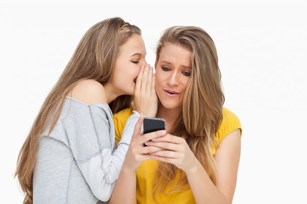 Estudante sussurando para sua amiga que texting em seu telefone