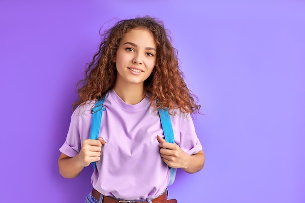 Estudante tímida e diligente, caucasiana, carregando uma bolsa escolar, posando para a câmera