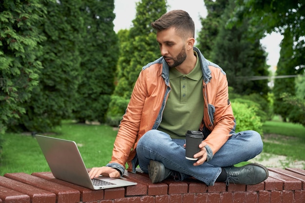 Estudante trabalhando no laptop com uma xícara de café no jardim