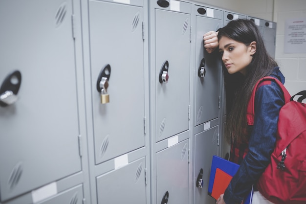 Estudante triste, apoiando-se no armário da universidade