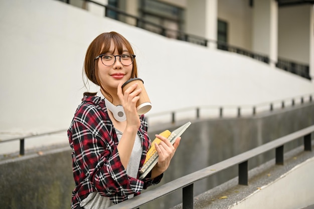 Estudante universitária asiática tomando café enquanto caminhava pelo prédio do campus