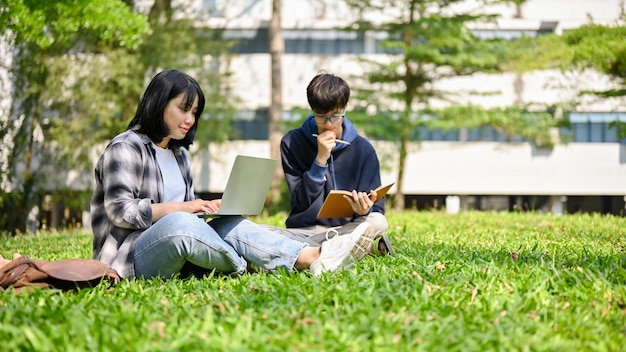 Estudante universitária asiática usando seu laptop enquanto está sentada no parque do campus com sua amiga