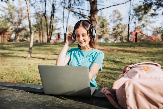Estudante universitária sorridente usando seu laptop no parque natural do campus. Conceito de e-learning.