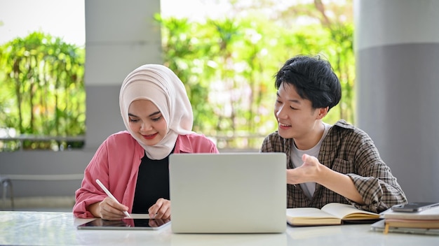 Estudante universitário asiático inteligente explicando e ensinando matemática para seu amigo muçulmano no campus