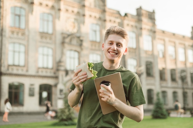 Estudante universitário bonito comendo sanduíche apetitoso