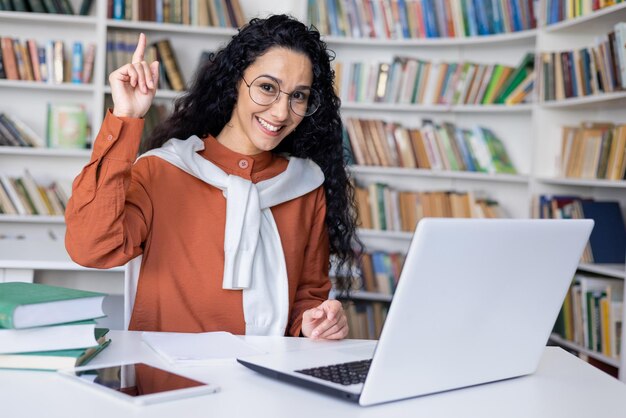 Foto estudante universitário encantado fazendo o gesto eureka enquanto estava sentado à mesa com o computador no fundo de