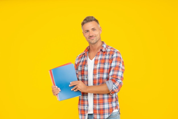 Estudante universitário feliz segurando livros para educação espaço de cópia de fundo amarelo